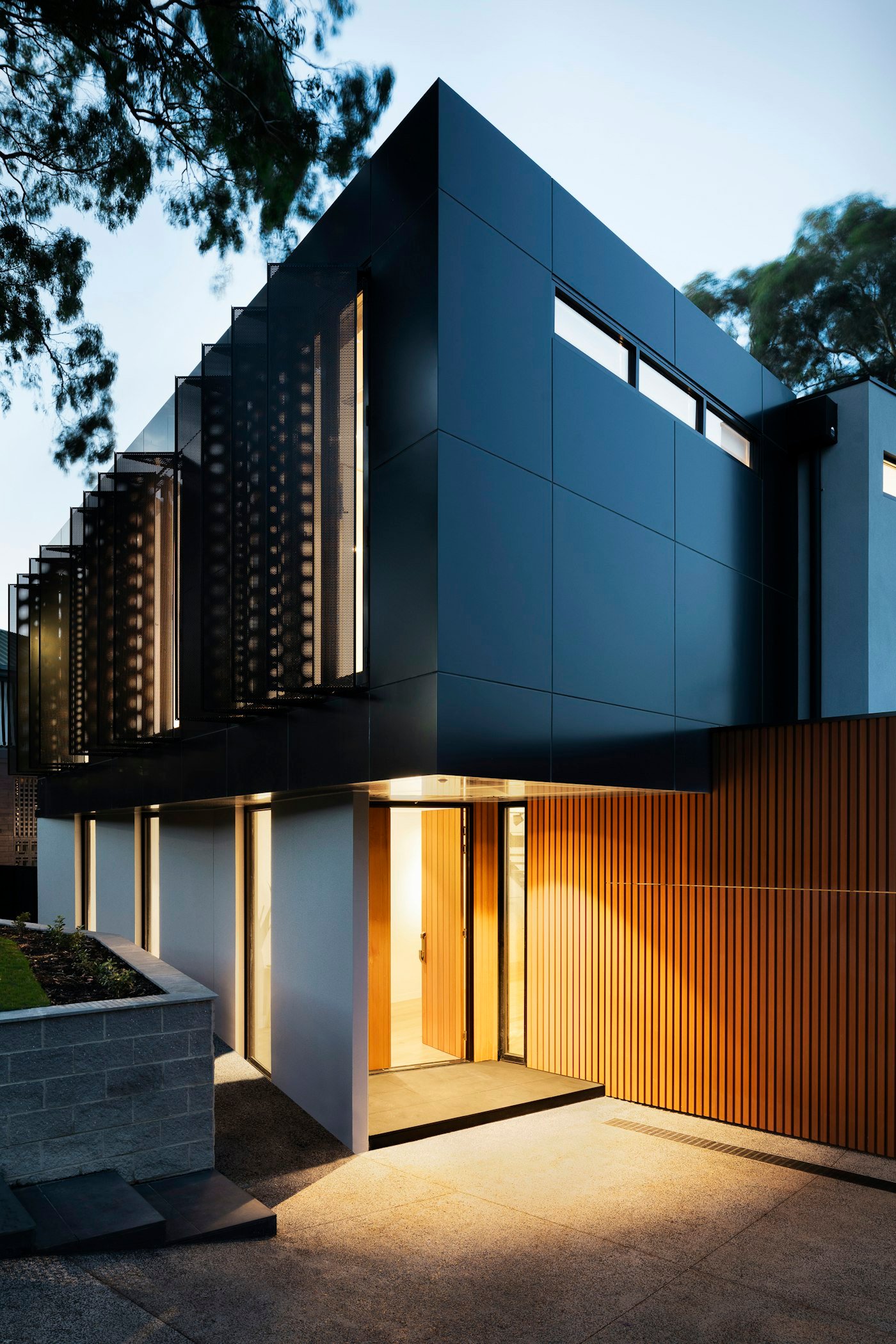 A modern entrance with dark metal panels, a warm timber door, and a lit timber wall