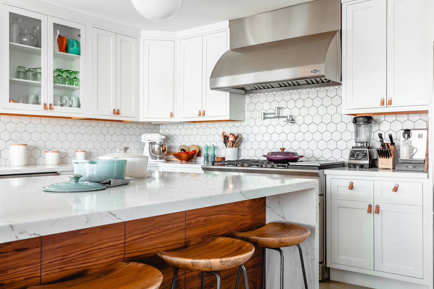 White kitchen with a marble island, wooden stools, a steel hood, and hexagonal tiles