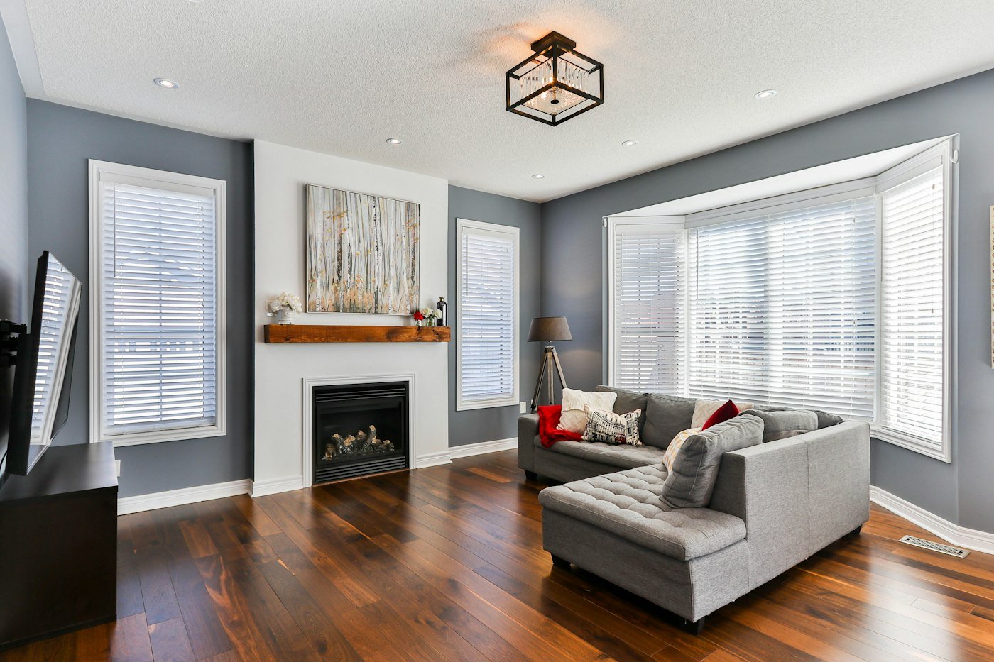 Grey living room with a corner sofa, white blinds, a black fireplace, and dark wood floors